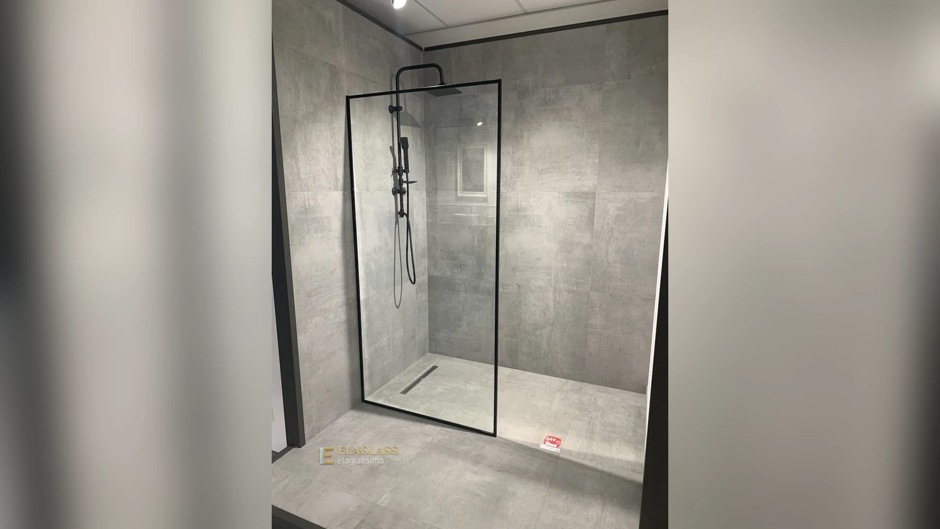 Paroi de douche en verre transparent avec cadre noir dans une salle de bain en pierre grise